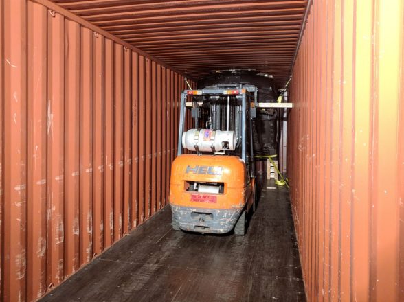 Forklift loading car into shipping container.